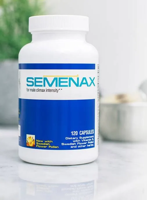 A man sitting in a bright room, holding the Semenax bottle in one hand